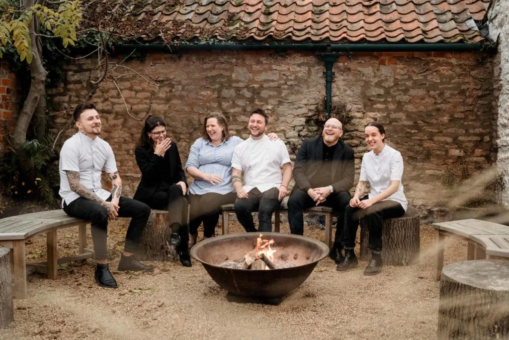 Staff members of Myse Restaurant sat outside near a garden firepit, in mid-conversation and laughing.